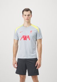 Light gray athletic shirt with yellow accents and red "L.F.C." and "AXA" logos. Made from breathable material, paired with dark shorts.