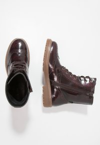 Botas de tobillo de charol burdeos con detalles de brogue, suelas de goma marrón, cordones en la parte delantera y cremallera lateral para facilitar su uso.