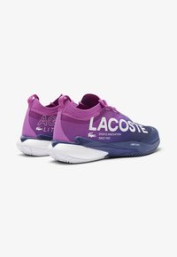 Sneakers Lacoste con un design sfumato viola e blu navy, con testo del logo bianco e suola in gomma texture per una migliore aderenza.