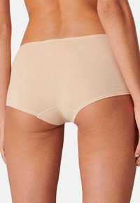 Sous-vêtements hipster beiges avec une texture lisse, une taille élastique et des bords sans coutures, conçus pour le confort et une visibilité minimale sous les vêtements.