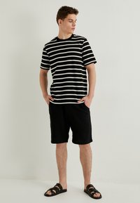 Sort og hvid stribet T-shirt parret med sorte teksturerede shorts, suppleret med sorte slidensandaler. Enkel design med en afslappet pasform.