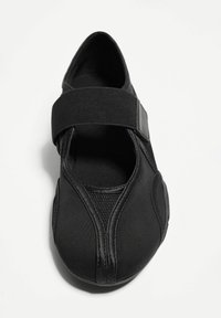 Pantof de sport negru, în stil Mary Jane, cu o curea elastică lată, superior din material moale și detalii texturate pe laturi.