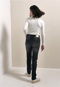 Czarne dżinsy w slim fit, z tylnymi kieszeniami i detalem w kolorze złotym. W zestawie z białą koszulą z długim rękawem i trampkami.