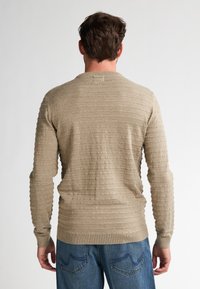 Beige strukturierter Pullover mit horizontalem Rippenmuster, langen Ärmeln und Rundhalsausschnitt, kombiniert mit blauen Jeans.