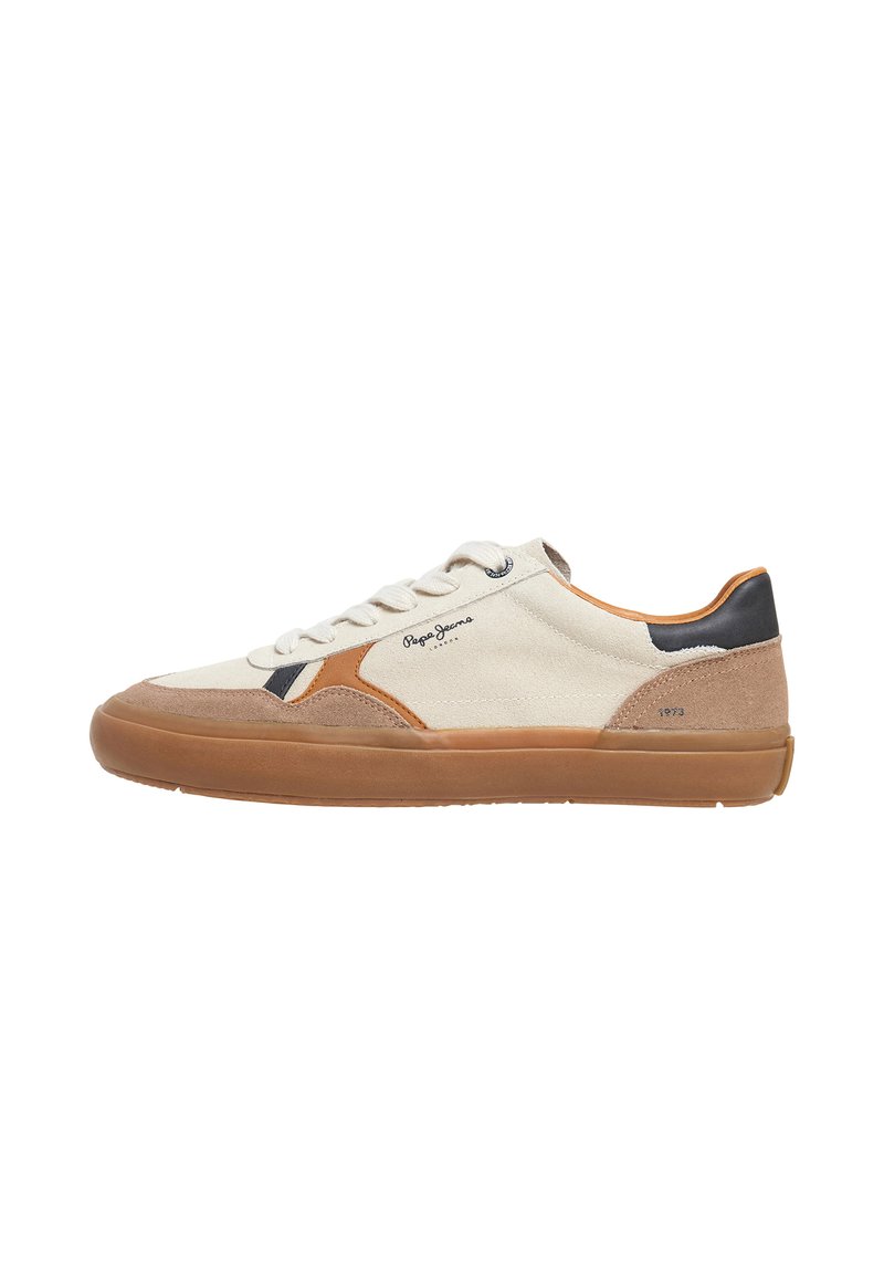 Zapatilla con parte superior de lona color crema, detalles en ante y cuero marrón, suela de goma y cordones blancos; presenta un logo y costuras decorativas.