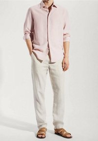 Camisa de manga larga rosa claro combinada con pantalones de lino de color claro y sandalias marrones con tiras, mostrando un ajuste relajado y un diseño sencillo.