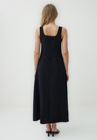 Czarna sukienka bez rękawów o prostym kroju, z kwadratowym dekoltem, zamkiem błyskawicznym z tyłu i szwami bocznymi dla dopasowanego wyglądu.