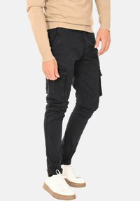Pantaloni cargo neri con vestibilità slim, dotati di tasche laterali, tessuto resistente e una finitura pulita. Abbinati a sneakers bianche.