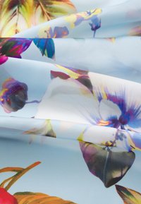 Il tessuto floreale presenta colori vivaci su uno sfondo azzurro chiaro. Include grandi petali e foglie, con una texture liscia e lucida.