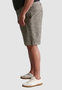 Gestreifte Khaki-Shorts mit seitlichen Taschen, taillierter Form und lockerer Passform. Kombiniert mit weißen Sneakers mit Gummisohle.