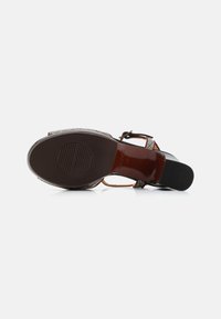 Black heel sandal with a patterned strap, smooth brown sole, and textured rubber outsole. Adjustable ankle strap with buckle.