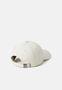 Beige hattu, joka on valmistettu puuvillasta, kaarevalla lippalakkosuunnittelulla, säädettävällä hihnalla takana ja huomaamattomalla logon brodeerauksella. Sileä pinta ja jämäkkä muotoilu.