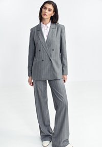 Szary marynarka w paski w podwójnym zapięciu z szerokimi spodniami w tym samym kolorze. Posiada guziki, klapy typu notch oraz jasnoróżową koszulę z kołnierzykiem pod spodem.