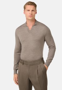 Hnědá polokošile s dlouhým rukávem a výstřihem do V, vyrobená z hladkého materiálu. Košile je kombinována s přizpůsobenými, skládacími tmavě hnědými kalhotami.