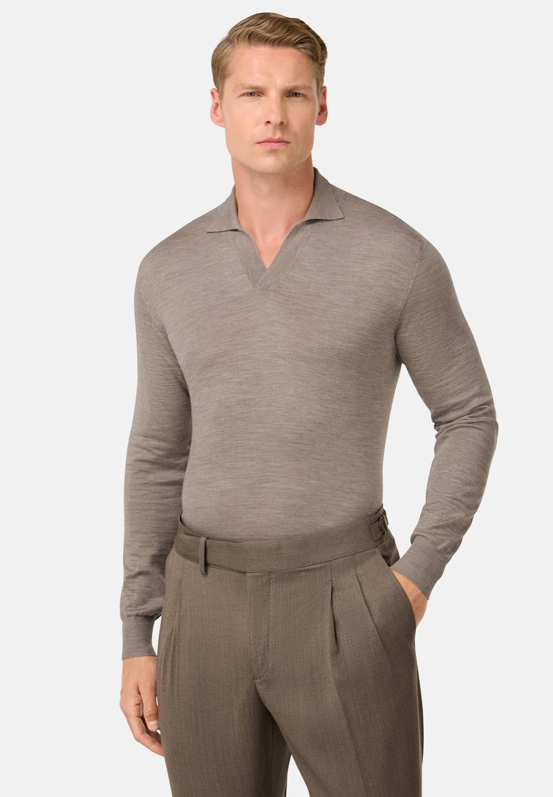 Hnědá polokošile s dlouhým rukávem a výstřihem do V, vyrobená z hladkého materiálu. Košile je kombinována s přizpůsobenými, skládacími tmavě hnědými kalhotami.