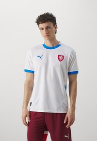 Balta sporta krekls ar zilu apkakli un piedurknēm, ar sarkanu Čehijas nacionālo emblēmu un nelielu Puma logotipu uz krūtīm.