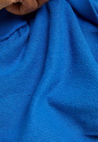 Un tejido azul texturizado muestra un sutil patrón acanalado, con una apariencia suave y tejida y un ligero brillo. La superficie es lisa y flexible.