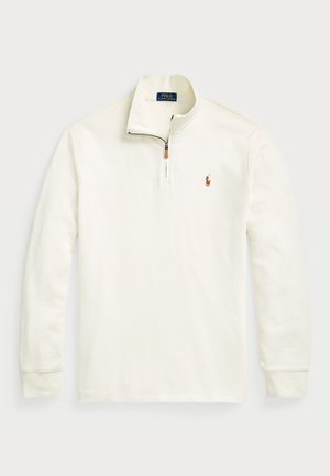Krämfärgad tröja med dragkedja i kragen, tillverkad av mjukt material. Har en liten broderad logotyp på vänster bröst. Långa ärmar.