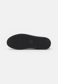Black rubber shoe sole with textured grip pattern, featuring a rectangular logo inset reading “CLAE.” Smooth edges and rounded shape.