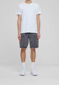 Valkoinen lyhythihainen t-paita, harmaat farkkushortsit repaleisella helmalla, joita on käytetty valkoisten tennareiden ja sukien kanssa. Yksinkertainen, rento muotoilu, jossa on vähän yksityiskohtia.