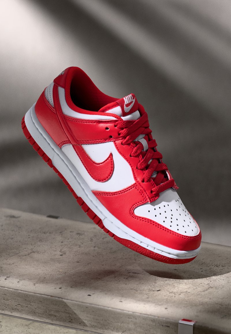 Piros és fehér Nike Dunk Low sneaker, bőr felsőrésszel, perforált orr résszel és textúrázott gumitalppal, kontrasztos részletekkel.