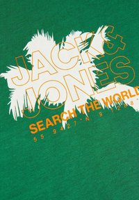 T-shirt verde in cotone con testo bianco e arancione: "JACK & JONES" e "SEARCH THE WORLD" con una grafica di palma e coordinate geografiche.