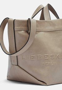 Torebka tote z brązowej skóry z dwoma krótkimi uchwytami, tłoczonym logo i kontrastowym czarnym przeszyciem; charakteryzuje się miękką, teksturowaną powierzchnią oraz geometrycznym wzorem.