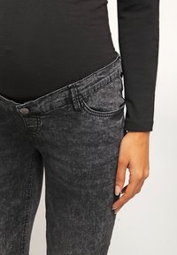 Jeans in denim grigio scuro con un design aderente, caratterizzati da uno stile a cinque tasche, sfumature sottili e una chiusura con bottone in vita.