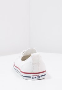 Białe płócienne sneakersy z zaokrąglonym czubkiem i płaską podeszwą. Posiadają czerwoną i niebieską paskowaną gumową podeszwę oraz logo na pięcie.