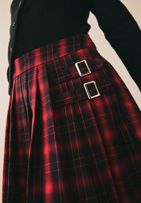 Červenočerná kostkovaná sukně z látky s nánosy, s dvojitými stříbrnými přezkami na pase pro detail a úpravu.