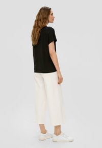 Zwart kort mouwtopje gecombineerd met brede, gecropte witte broeken. De outfit wordt compleet gemaakt met witte sneakers, die een gladde textuur en eenvoudig ontwerp hebben.