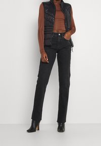 Musta toppaliivi sik-sak-tikkauksilla, yhdistetty ruskeaan pitkähihaiseen puseroon ja mustiin suoralahkeisiin farkkuihin, viimeistelty mustilla korkokengillä.