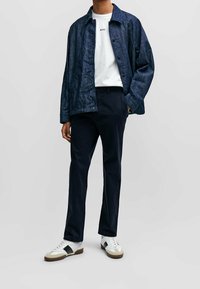 Marinblå linnjacka, vit t-shirt med text, marinblå byxor och vita sneakers med svarta accenter. Avslappnad, moderne passform.