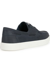 Zapato deslizante de cuero marino con acabado texturizado, suela de goma blanca y detalles de costura sutiles. Diseño de punta redonda y silueta de bajo perfil.