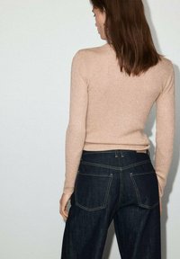 Maglione a maglia beige chiaro con texture a coste abbinato a jeans in denim blu scuro a vita alta con cuciture visibili e due tasche posteriori.