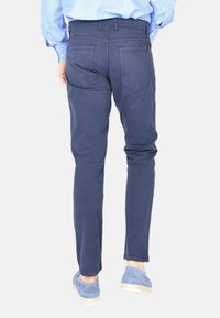 Chino slim-fit blu navy in cotone con una texture liscia, dotati di tasche posteriori e cuciture pulite. Abbinati a scarpe blu.