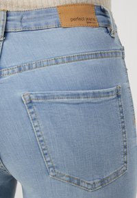 Jeans de mezclilla azul claro con una parche de cuero marrón con la marca en la parte trasera de la cintura, que cuentan con dos bolsillos traseros y detalles de costura visibles.