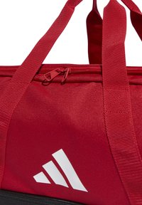 Bolsa de deporte roja con acabado texturizado, cuenta con dos asas superiores, cierre de cremallera y detalle del logotipo blanco en el lateral. Diseño duradero.
