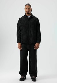 Zwarte corduroy overshirt met een kraag, gecombineerd met loszittende zwarte spijkerbroeken en zwarte stevige schoenen met roze veters.