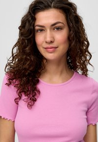 Różowa, prążkowana bluzka z krótkim rękawem, okrągłym dekoltem i falbanowym wykończeniem. Tkanina jest gładka, co zapewnia dopasowany krój.