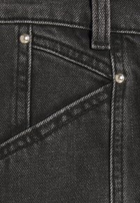 Pantalones de mezclilla negros con botones plateados y un patrón de costura prominente. Primer plano de los bolsillos y detalle de la textura en la tela.