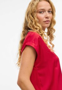 Top rosso a maniche corte in tessuto liscio con una vestibilità comoda. Presenta risvolti sulle maniche e un collo rotondo, caratterizzato da un colore uniforme senza pattern.