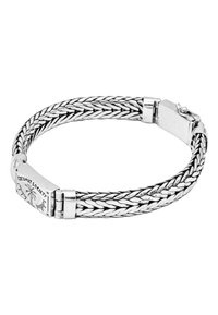 Silverflätad armband med en slät metallspänne. Har graverad logotyp på spännet. Reflekterande metalltextur genom hela armbandet.