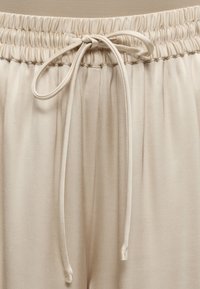 Μπεζ παντελόνια με ελαστική μέση και δεμένο κορδόνι στο κέντρο μπροστά, κατασκευασμένα από λείο, ελαφρύ ύφασμα.