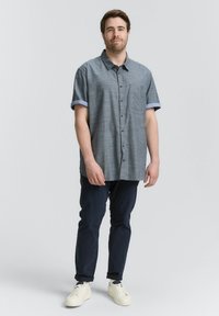 Korte mouwen, blauwe blouse met kraag en een gestructureerde afwerking, met donkere knopen en opgerolde mouwen, gecombineerd met marineblauwe broek en witte sneakers.