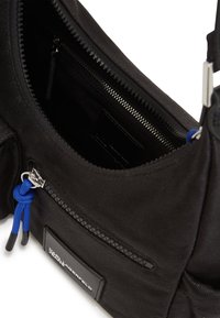 Black fabric crossbody bag featuring a zipper closure, blue cord accents, and a front pocket with a branded label. Textured, durable material.