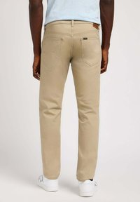Beige chino's met een rechte snit, voorzien van achterzakken en een leren logo-label op de tailleband, gecombineerd met witte sneakers.