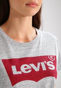 Grå bomulds t-shirt med et stort rødt Levi's-logo i en karakteristisk buet form. Rund hals, korte ærmer, med en blød tekstur.