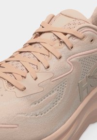 Κοντινό πλάνο ενός μπεζ αθλητικού παπουτσιού με ύφασμα από δίχτυ, κορδόνια στο ίδιο χρώμα και διακριτική ανάγλυφη σήμανση στη πλευρά.