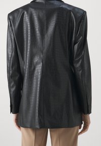 Blazer en similicuir noir avec une texture crocodile, doté d'une coupe droite, de manches longues et de poignets boutonnés. Design épuré et minimaliste.